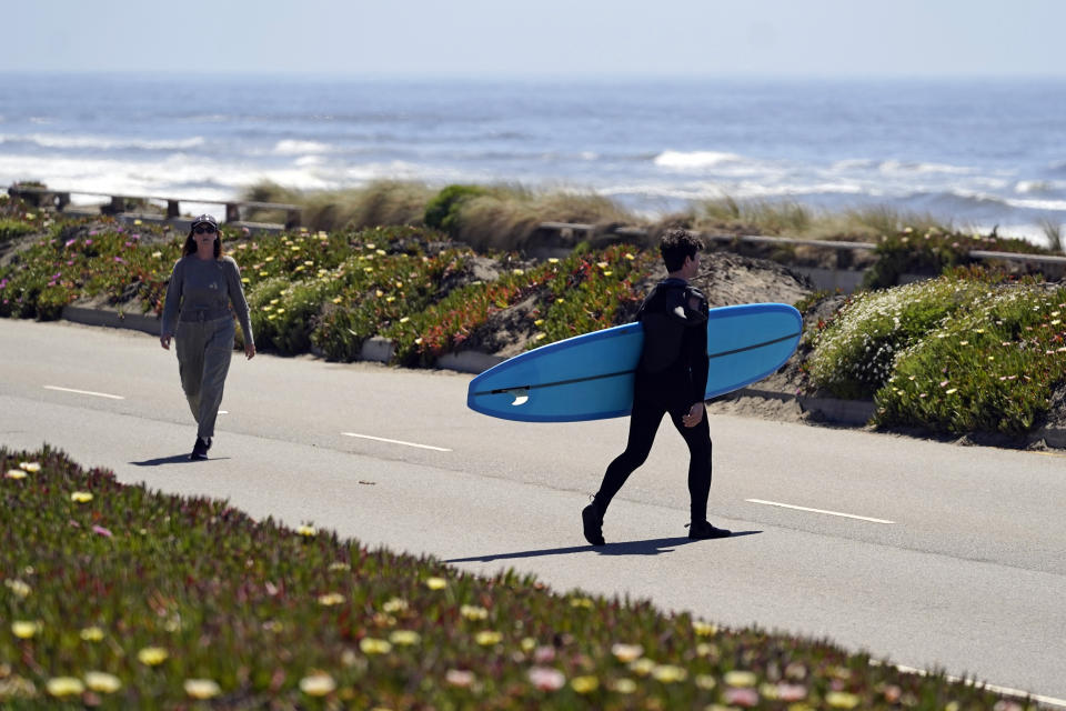 A surfer walks with his board across the car-free Great Highway toward the ocean in San Francisco, on April 28, 2021. At the start of the pandemic, San Francisco closed off parts of a major beachfront highway and Golden Gate Park to cars so that people had a safe place to run and ride bikes. Open space advocates want to keep those areas car-free as part of a bold reimagining of how U.S. cities look. But opponents decry the continued closures as elitist, unsafe and nonsensical now that the pandemic is over and people need to drive again. (AP Photo/Eric Risberg)