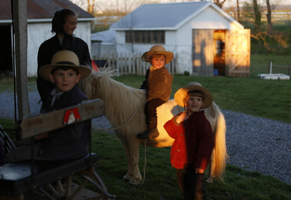 In this Monday, May 4, 2020, photo, three-year-old Lewis, center, sits on a miniature horse as he plays with his siblings and other area children at his home in Ephrata, Pa. The children attend the Old Order Stauffer Mennonite Church with more than 200 hundred other community members in the Mennonite Valley of Lancaster County. (AP Photo/Jessie Wardarski)