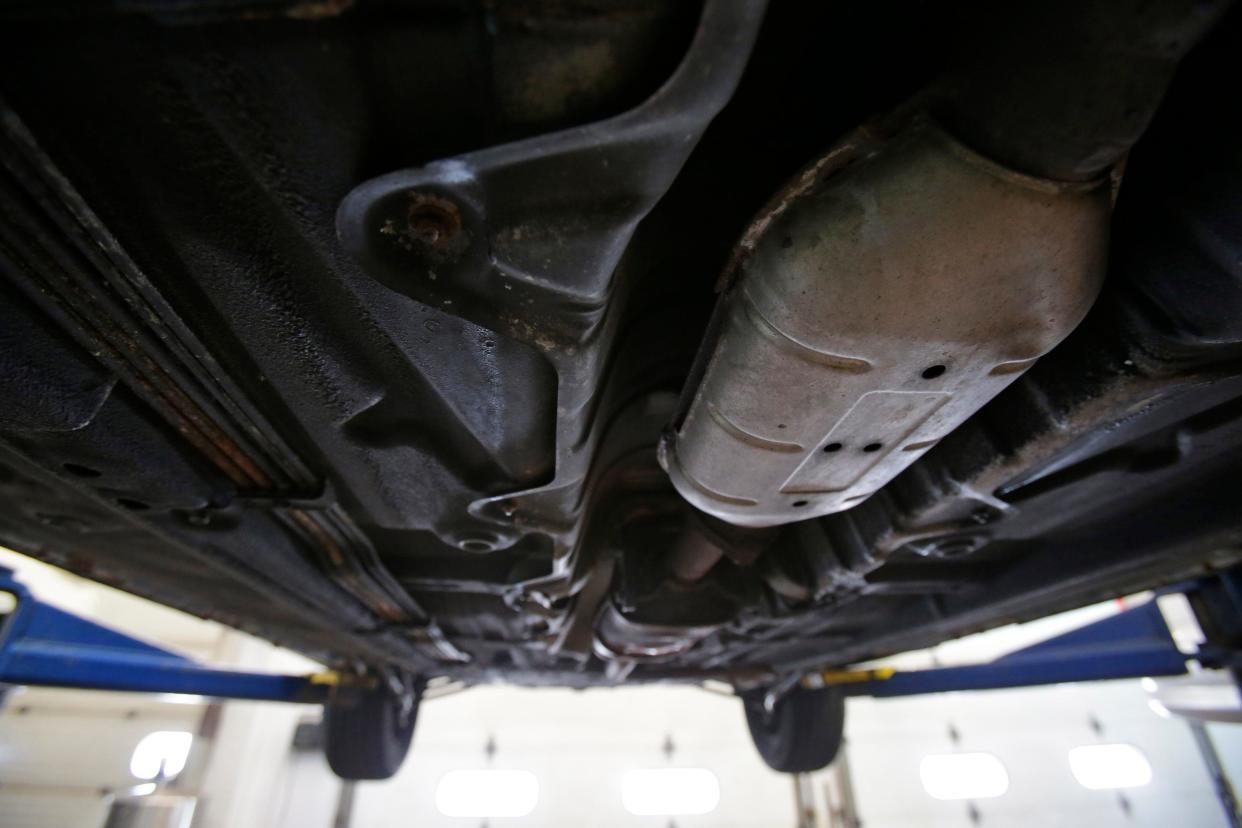 A catalytic converter is shown under a car on a lift. The devices, which convert toxic gases into more benign emissions, are often the target of thieves because they contain precious metals, including platinum.