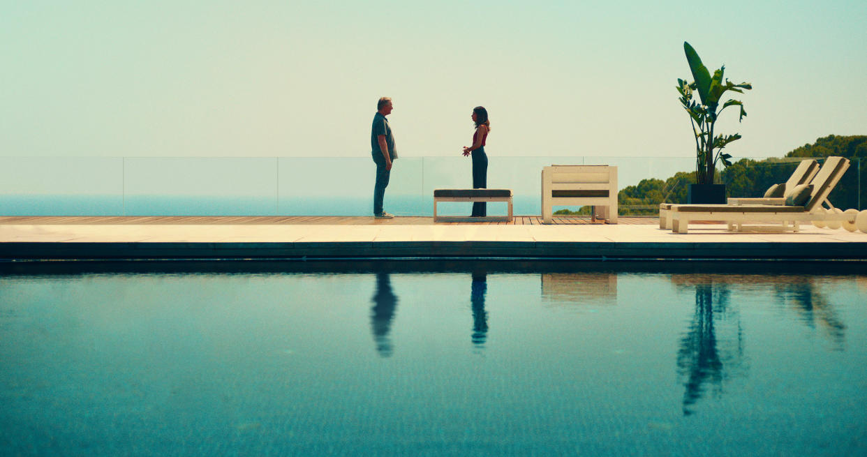  Daniel Lang (Douglas Henshall) and Erin Carter (Evin Ahmad) stand facing each other on the far side of a gloriously blue swimming pool, with the ocean visible behind a low glass wall behind them 