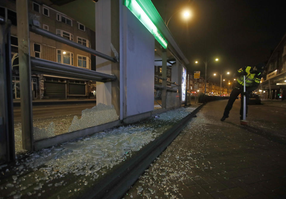A police officer sweeps up glass from a bus stop that was smashed in protests against a nation-wide curfew in Rotterdam, Netherlands, Monday, Jan. 25, 2021. The Netherlands Saturday entered its toughest phase of anti-coronavirus restrictions to date, imposing a nationwide night-time curfew from 9 p.m. until 4:30 a.m. in a bid to control the COVID-19 infection rate. (AP Photo/Peter Dejong)