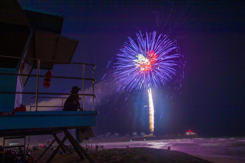 Huntington Beach, CA - July 04: Huntington Beach lifeguards watch the fireworks display over the ocean at the pier on the Fourth of July Sunday, July 4, 2021 in Huntington Beach, CA. A Pier Plaza Festival featured live entertainment & DJs, merchant & crafts vendor booths, amusements & carnival rides, food trucks, beer & wine garden, sponsor activations, live radio broadcasts, and prize giveaways. A Surf City Run 5K kicked off the day and a neighborhood parade that included 3 separate routes replaced the large parade of year's past before the pandemic. The grand finale featured fireworks over the ocean shot off from the pier at 9pm. (Allen J. Schaben / Los Angeles Times)