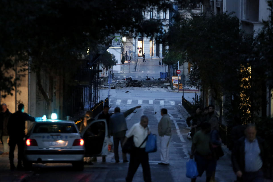 The remains of a car sits on a street after a car bomb explosion in central Athens as police officers block the street on Thursday, April 10, 2014. The bomb exploded outside a Bank of Greece building in central Athens before dawn Thursday, causing some damage but no injuries. The blast came hours before Greece was to return to the international bond markets for the first time in four years, and a day before German Chancellor Angela Merkel was to visit Athens.(AP Photo/ Petros Giannakouris)