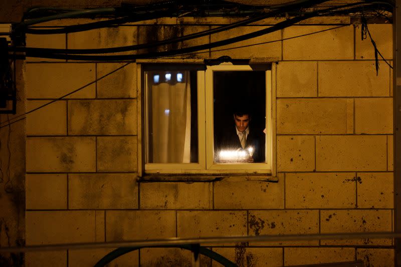 A Jewish seminary student is seen through his window as he lights a hanukkiyah, a candlestick with nine branches that is lit to mark Hanukkah, the 8-day Jewish Festival of Lights, in Bnei Brak, Israel