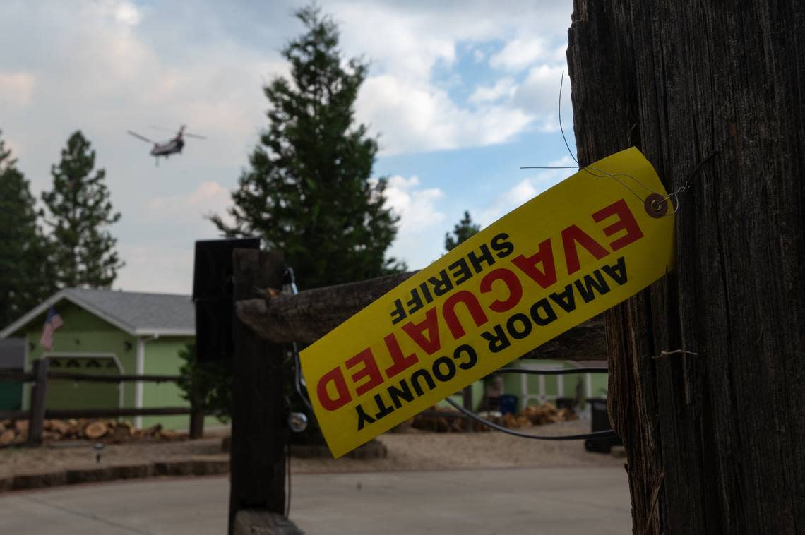 A tag from the Amador County Sheriff’s Office indicates that the residents of a home have evacuated inside the mandatory evacuation zone for the Electra Fire in Pine Grove on Tuesday evening, July 5, 2022, as a Chinook fire fighting helicopter flies above the threatened structures.