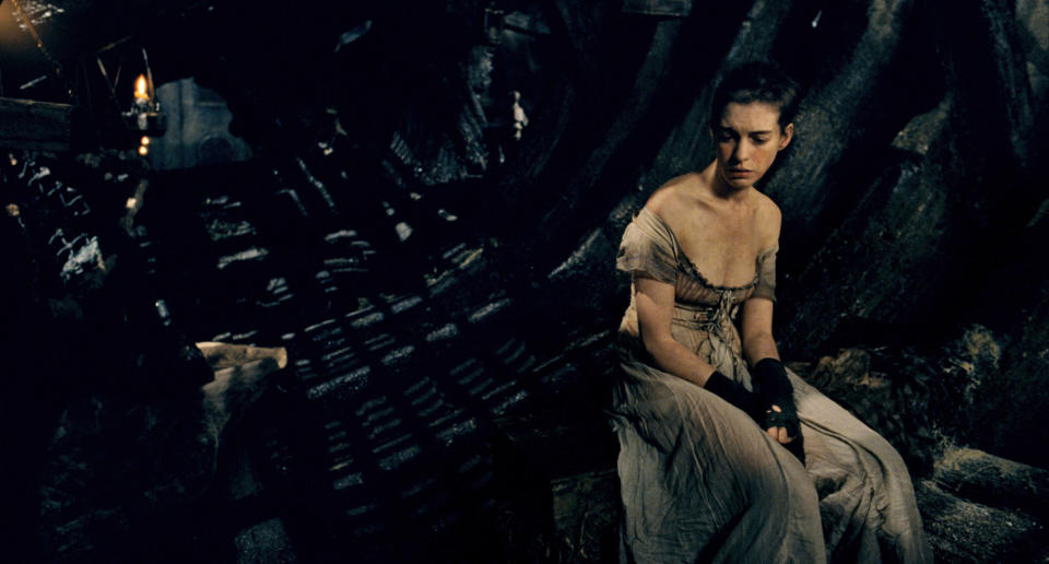 Anne as Fantine in a gown, sitting and looking sad