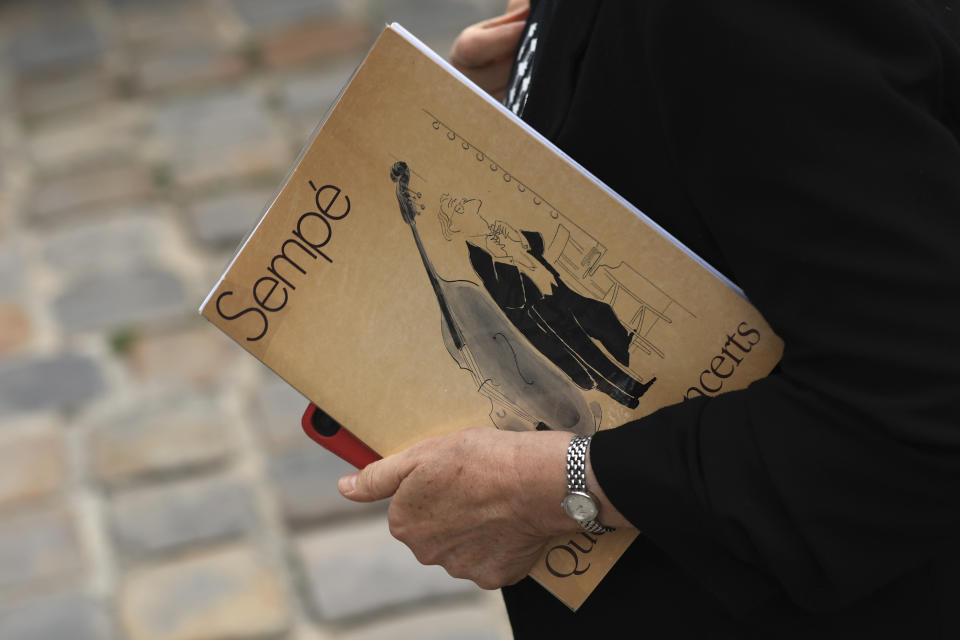 A woman holding a notebook with a drawing by Sempe arrives at Jean-Jacques Sempe's funeral ceremony at the Saint-Germain-des-Pres church in Paris, Friday, Aug.19, 2022. Cartoonist Jean-Jacques Sempe, whose simple line drawings captured French life and won international acclaim on the covers of New Yorker magazine, has died on Aug.11, 2022. He was 89. (AP Photo/Aurelien Morissard)