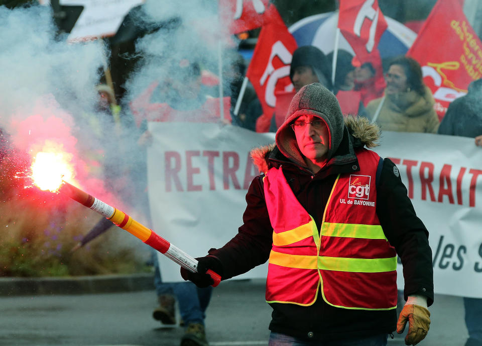 A trade union demonstrator holds a flare, during a protest in Bayonne, southwestern France, Thursday, Dec. 12, 2019. France's prime minister said Wednesday that the full retirement age will be increased for the country's youngest, but offered concessions in an ill-fated effort to calm a nationwide protest against pension reforms that critics say will erode the nation's way of life. (AP Photo/Bob Edme)