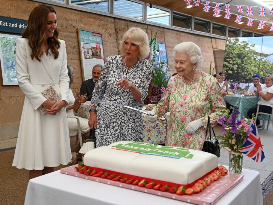 Queen Elizabeth cuts a cake with a sword as Kate Middleton and Camilla look on