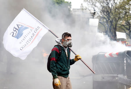 A protesters holds a flag of Argentina's Rio Santiago shipyard as he stands amidst smoke during clashes with the police outside the Congress, where the budget bill is being debated, in Buenos Aires, Argentina October 24, 2018. REUTERS/Martin Acosta