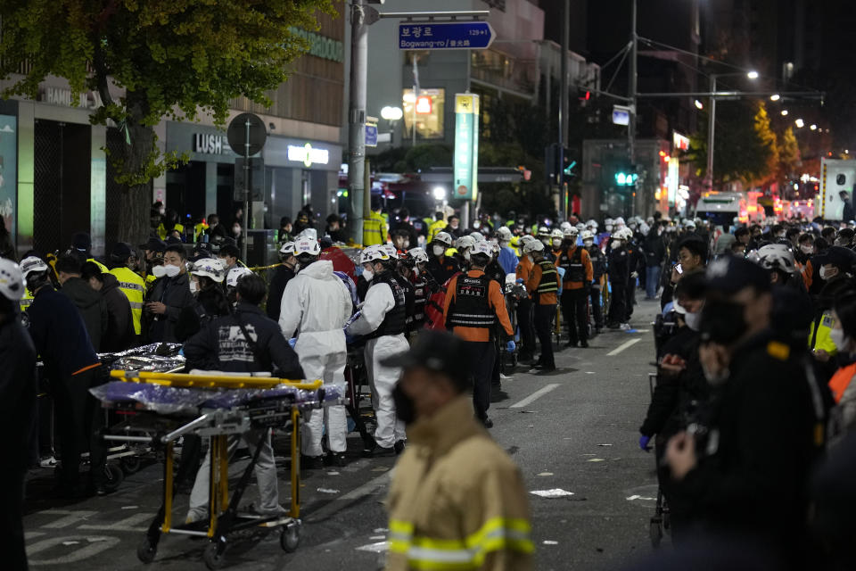Rescue workers wait to carry victims near the scene where scores of people died and were injured in Seoul, South Korea, Sunday, Oct. 30, 2022. Witnesses say the nightmarish scene intensified as people performed CPR on the dying and carried limp bodies to ambulances, while dance music pulsed from garish clubs lit in bright neon. Others tried desperately to pull out those who were trapped underneath the crush of people, but failed because too many in the crowd had fallen on top of them. (AP Photo/Lee Jin-man)