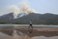 A man walks on the beach with a wildfire burning the forest in Turgut village, near tourist resort of Marmaris, Mugla, Turkey, Wednesday, Aug. 4, 2021. As Turkish fire crews pressed ahead Tuesday with their weeklong battle against blazes tearing through forests and villages on the country's southern coast, President Recep Tayyip Erdogan's government faced increased criticism over its apparent poor response and inadequate preparedness for large-scale wildfires.(AP Photo/Emre Tazegul)