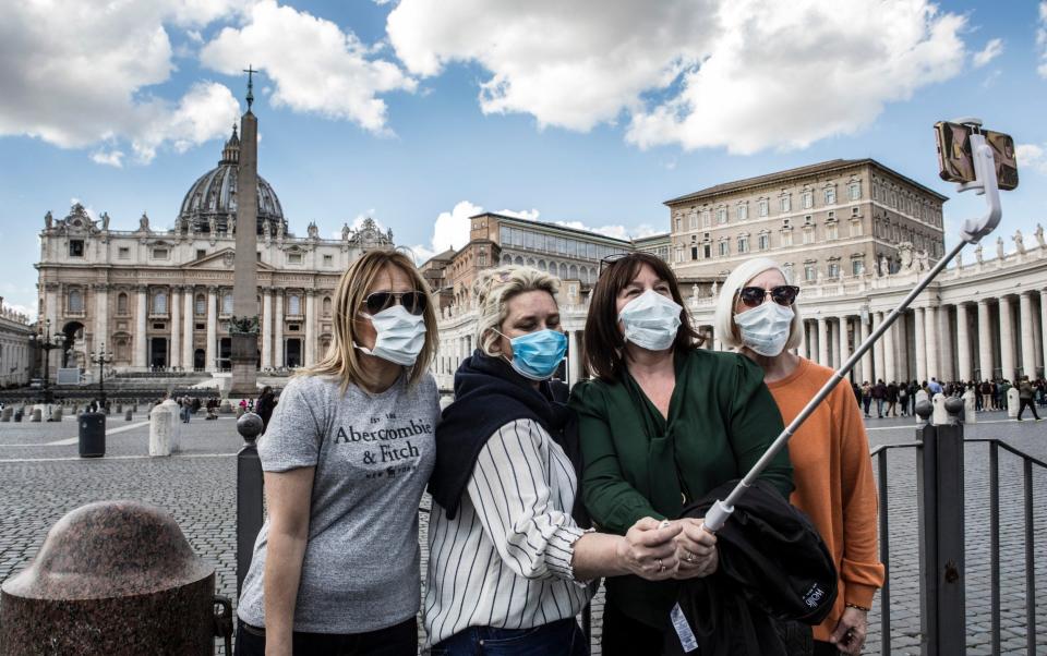 Tourists wearing protective masks take selfies in Peter's Square