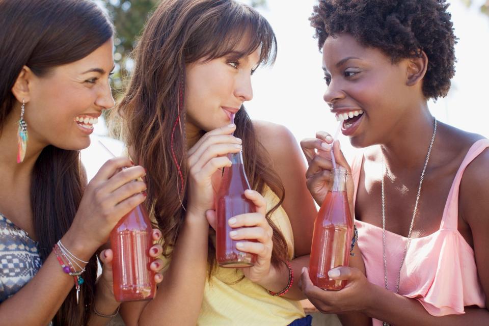 Three friends enjoying a bottled beverage together.