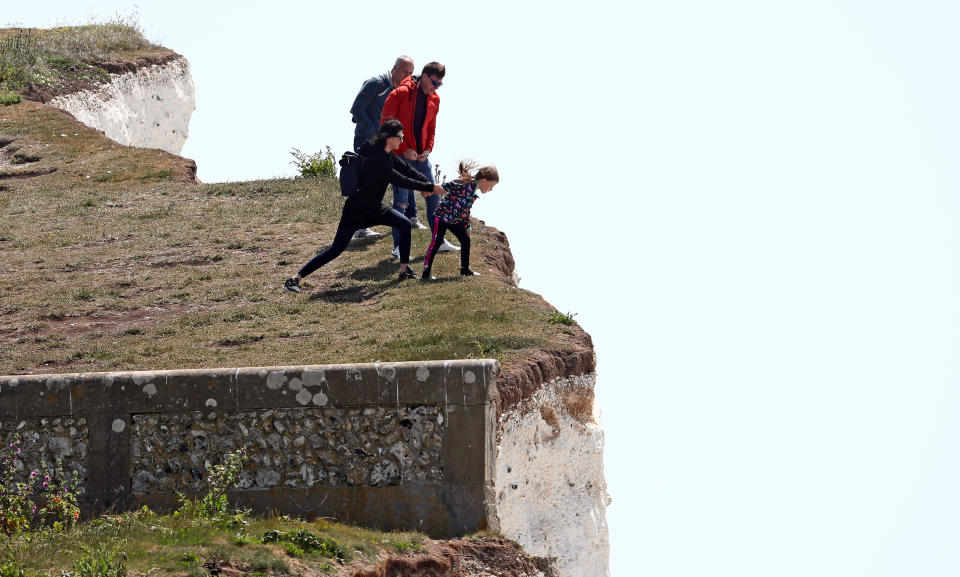 A young girl is held back as she peers over the edge of cliffs at Birling Gap.