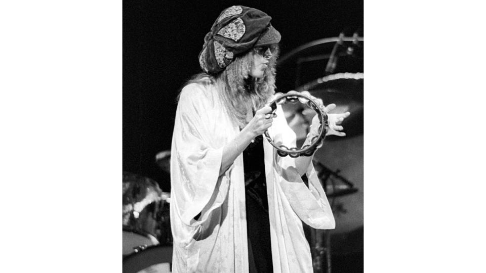 Stevie Nicks wearing hat and kimono while playing tamberine.