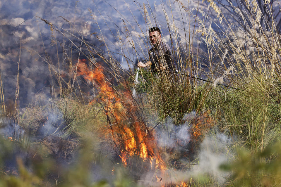 A member of anti-forest fire team puts out flames burning in Capaci, near Palermo, in Sicily, southern Italy, Wednesday, July 26, 2023. On the island of Sicily, two people were found dead Tuesday in a home burned by a wildfire that temporarily shut down Palermo's international airport, according to Italian news reports. Regional officials said 55 fires were active on Sicily, amid temperatures in the 40s Celsius. (Alberto Lo Bianco/LaPresse via AP)