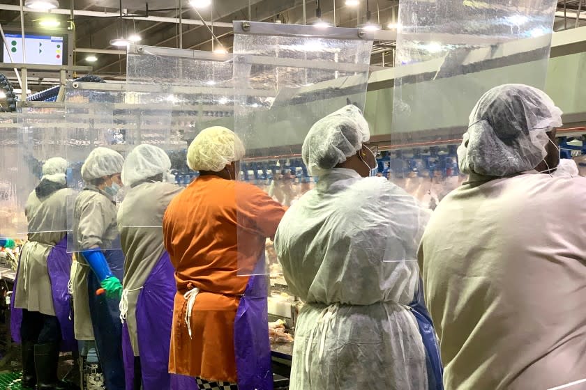 In this April 2020, photo provided by Tyson Foods, workers wear protective masks and stand between plastic dividers at the company's Camilla, Georgia poultry processing plant. Tyson has added the plastic dividers to create separation between workers because of the coronavirus outbreak. (Tyson Foods via AP)