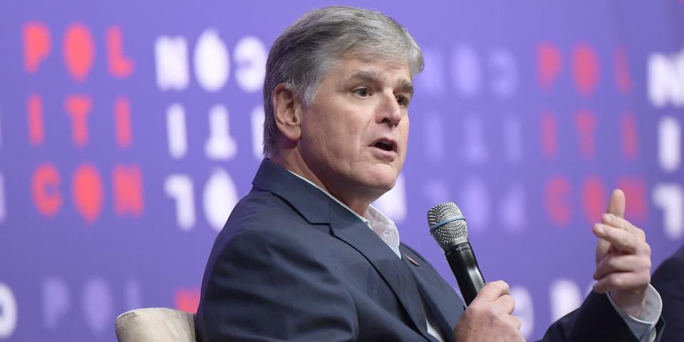 Sean Hannity points at himself while holding a microphone.