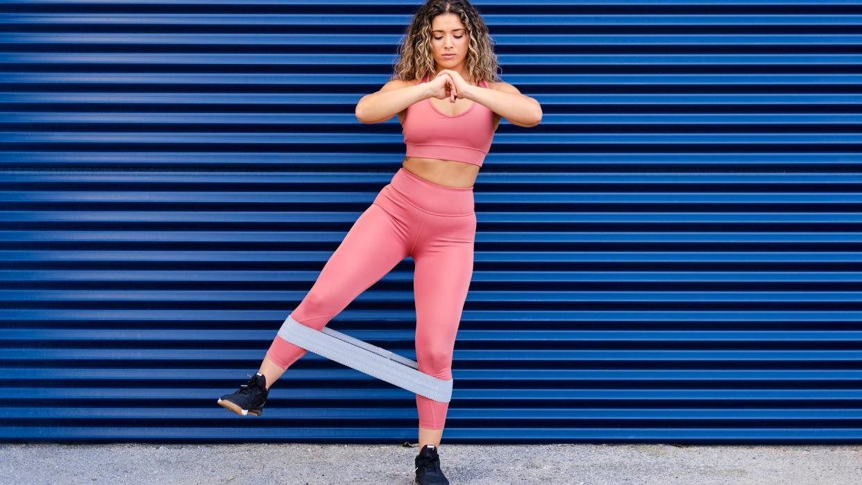  A woman in pink fitness clothes exercising her legs with a an exercise band 