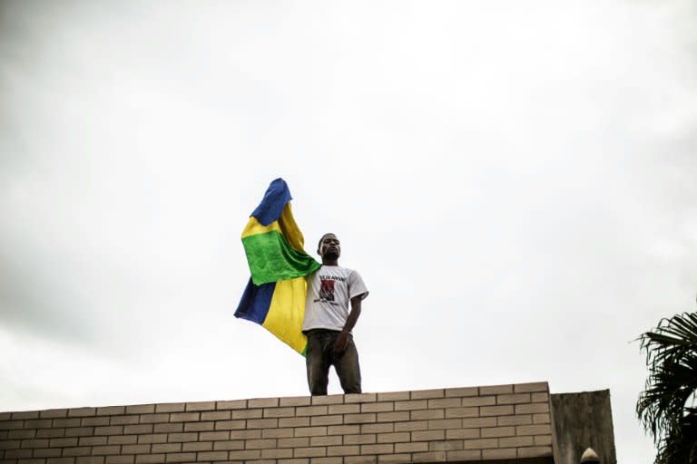 A supporter stands on a roof as he holds the Gabonese national flag in the headquarter of the opposition leader Jean Ping in Libreville on August 30, 2016