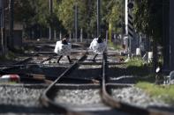 <p>Straßenhändler im griechischen Athen tragen während eines Eisenbahnstreiks ihre Güter über die Eisenbahnschienen. Alle Bahnstrecken in Griechenland wurden wegen eines Streiks gegen Privatisierung und für mehr Personal für 24 Stunden lahmgelegt. (Bild: AP Photo/Petros Giannakouris) </p>