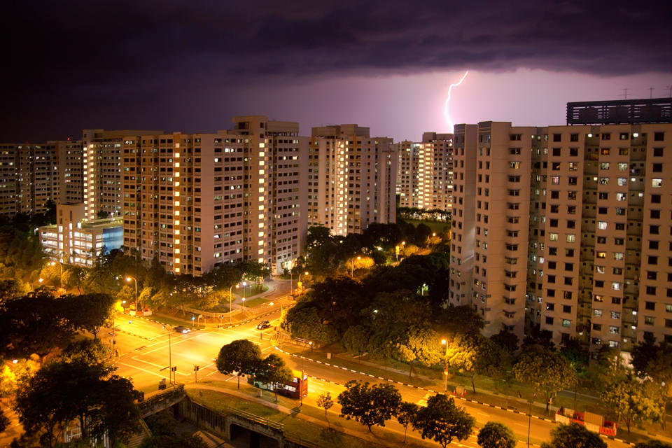 Lightning strikes over HDB flats in Jurong West, Singapore, illustrate the story of falling electricity tariffs.