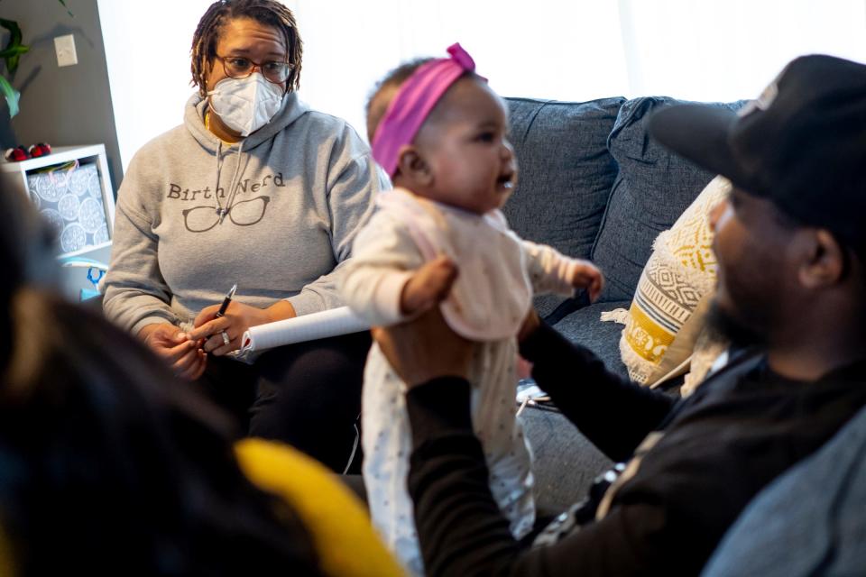 Doula Erika Millender, left, talks with DeJuan Bland as he holds his daughter Wynter Bland, 4 months while sitting with his wife Jenise Bland during a post-natal visit to their home in Dearborn on January 12, 2023. Doulas serve birthing people prenatally, during labor and delivery and after a baby is born. Clients typically pay out of pocket for doula services, which have been proven to improve maternal and infant health outcomes. Effective Jan. 1, Michigan Medicaid will reimburse doulas for their services. The state says it's in part an effort to increase equity and address racial disparities. Doulas see the policy as a positive validation of their work but are disappointed by the relatively low rate at which Medicaid will reimburse.