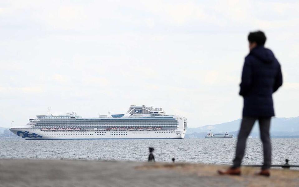 A member of the media looks out toward the Diamond Princess cruise ship (L) with over 3,000 people as it sits anchored in quarantine off the port of Yokohama on February 4, 2020, a day after it arrived with passengers feeling ill. - Japan has quarantined the cruise ship carrying 3,711 people and was testing those onboard for the new coronavirus on February 4 after a passenger who departed in Hong Kong tested positive for the virus. (Photo by Behrouz MEHRI / AFP) (Photo by BEHROUZ MEHRI/AFP via Getty Images)