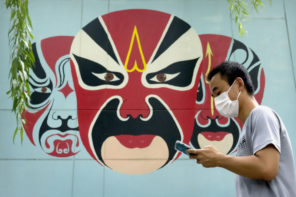 A man wearing a face mask to protect against the spread of COVID-19 walks past a mural depicting traditional opera face makeup in Beijing, Friday, Aug. 13, 2021. (AP Photo/Mark Schiefelbein)