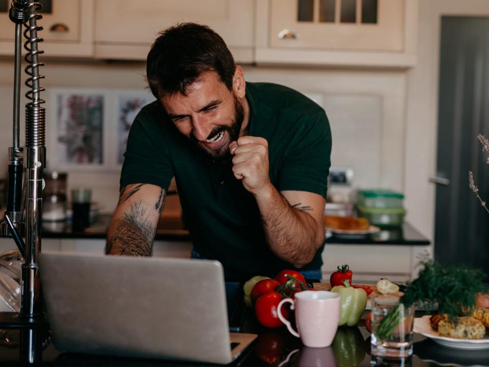 Man in a kitchen looking happy over a laptop