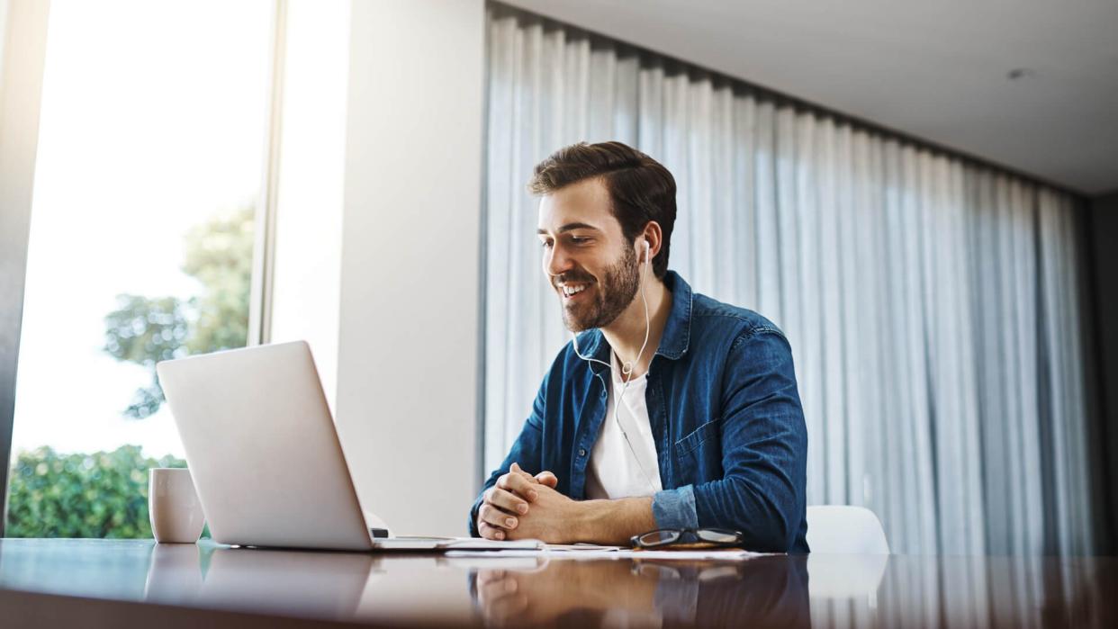 Shot a handsome young businessman sitting down and using his laptop to take a video call while working from home.