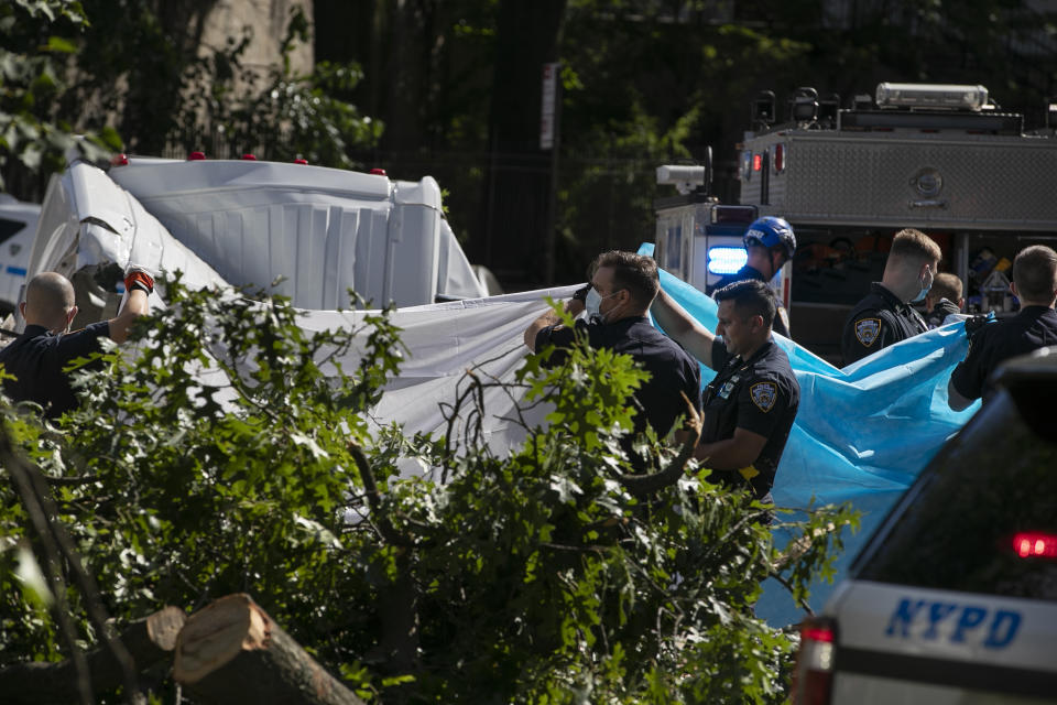 New York City Police officers shield a person from view who died after a tree fell on a van as Tropical Storm Isaias moved past New York, Tuesday, Aug. 4, 2020, in New York. (AP Photo/Frank Franklin II)