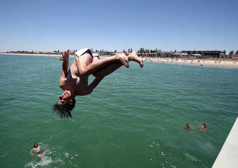 Teenagers leap from the Henley Beach Jetty during a hot day in Adelaide.