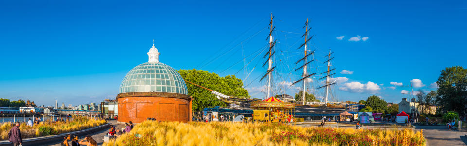 Crowds of people enjoying the summer sunshine beside the historic Cutty Sark and Greenwich Foot Tunnel at Maritime Greenwich, London, UK.