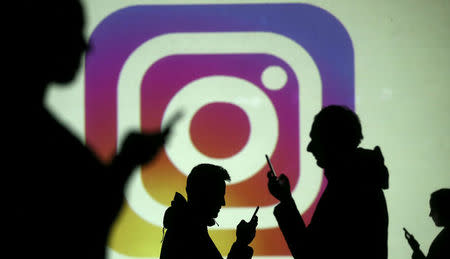 FILE PHOTO: Silhouettes of mobile users are seen next to a screen projection of Instagram logo in this picture illustration taken March 28, 2018. REUTERS/Dado Ruvic/Illustration