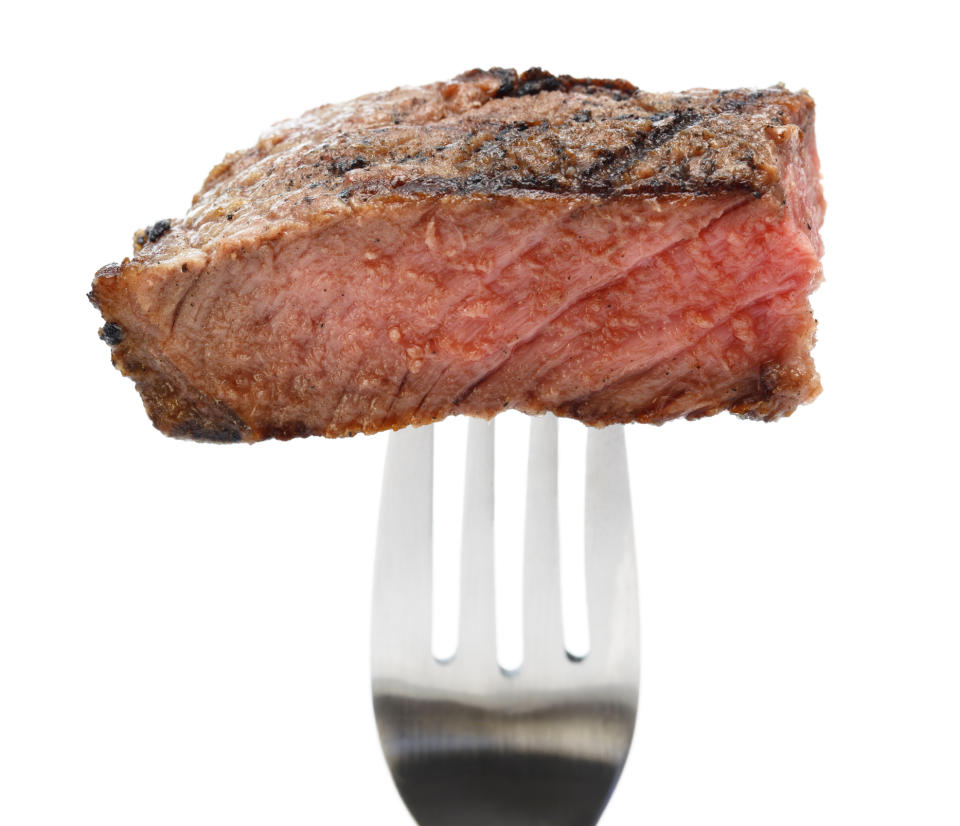 A juicy, medium-rare piece of steak is shown pierced by a fork against a white background