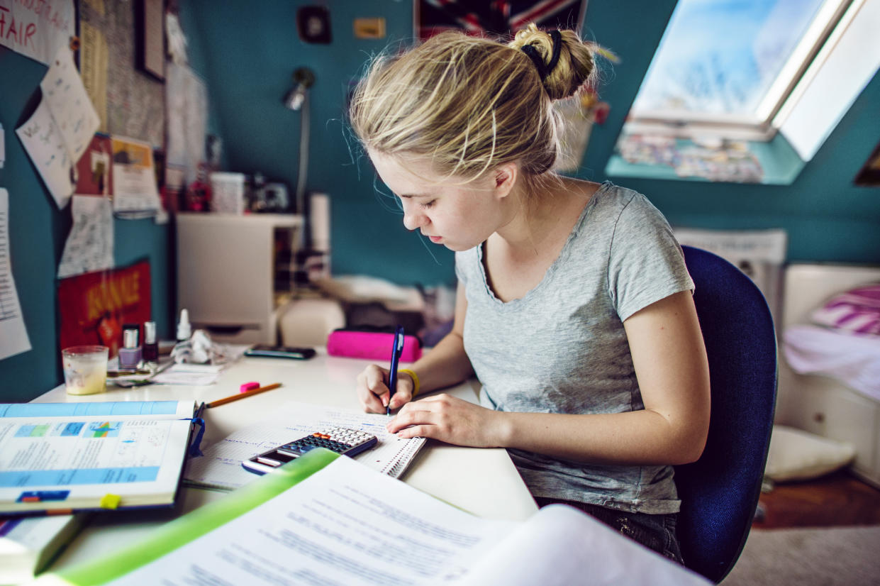 Young woman with blonde hair, sitting at a desk in her room and doing maths-homeworks