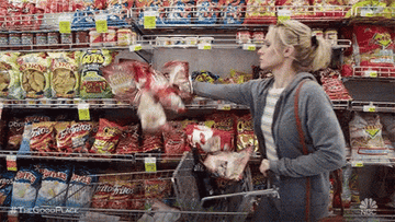 A woman throwing bags of chips into her grocery store basket