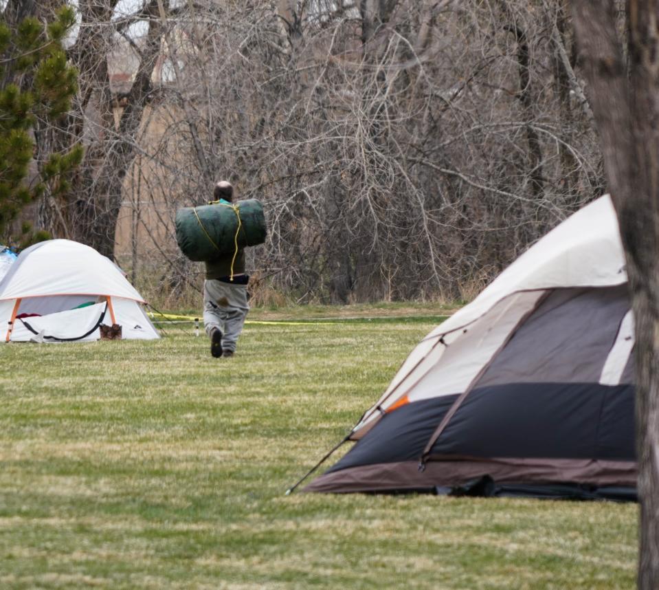 A man ordered to leave an encampment outside a temporary shelter for people experiencing homelessness in Fort Collins, Colorado, walks toward a wooded area to cache his belongings.