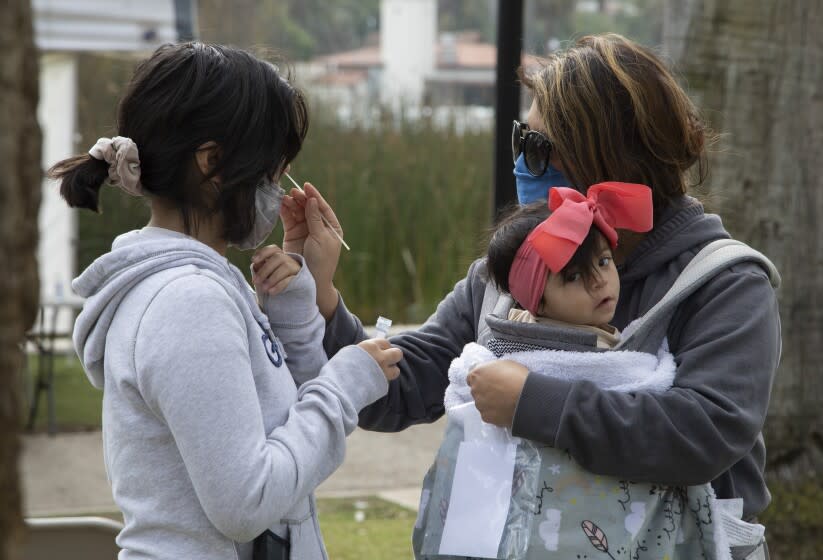 LOS ANGELES, CA - JANUARY 18: Veronica Francisco, right, holding 9-month-old Alayla, swabs her daughter Abigail Campos, 11, during free COVID-19 testing at Echo Park on Tuesday, Jan. 18, 2022. The site was moved from Reservoir Street to provide a ``more convenient user experience'' amid a surge in COVID-19 cases related to the Omicron variant, Councilman Mitch O'Farrell said in an email to constituents Saturday. (Myung J. Chun / Los Angeles Times)