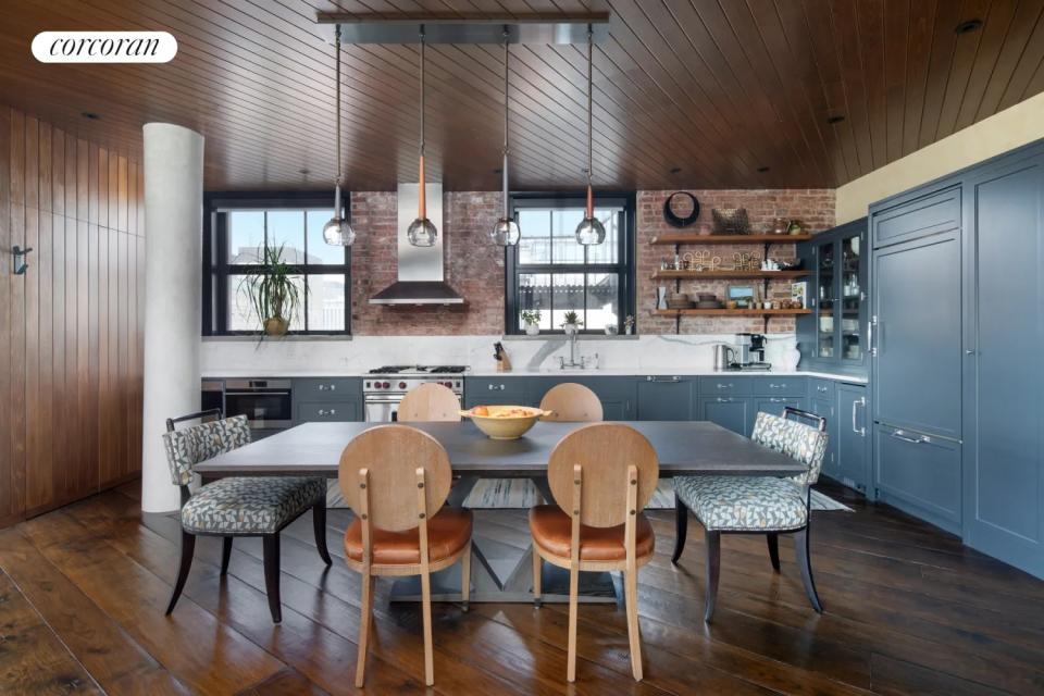 An open plan kitchen with gray-blue cabinets in an industrial style apartment with exposed brickwork and concrete columns