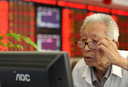 An investor adjusts his glasses as he looks at a computer screen in front of an electronic board showing stock information at a brokerage house in Fuyang, Anhui province, China, July 9, 2015. REUTERS/China Daily