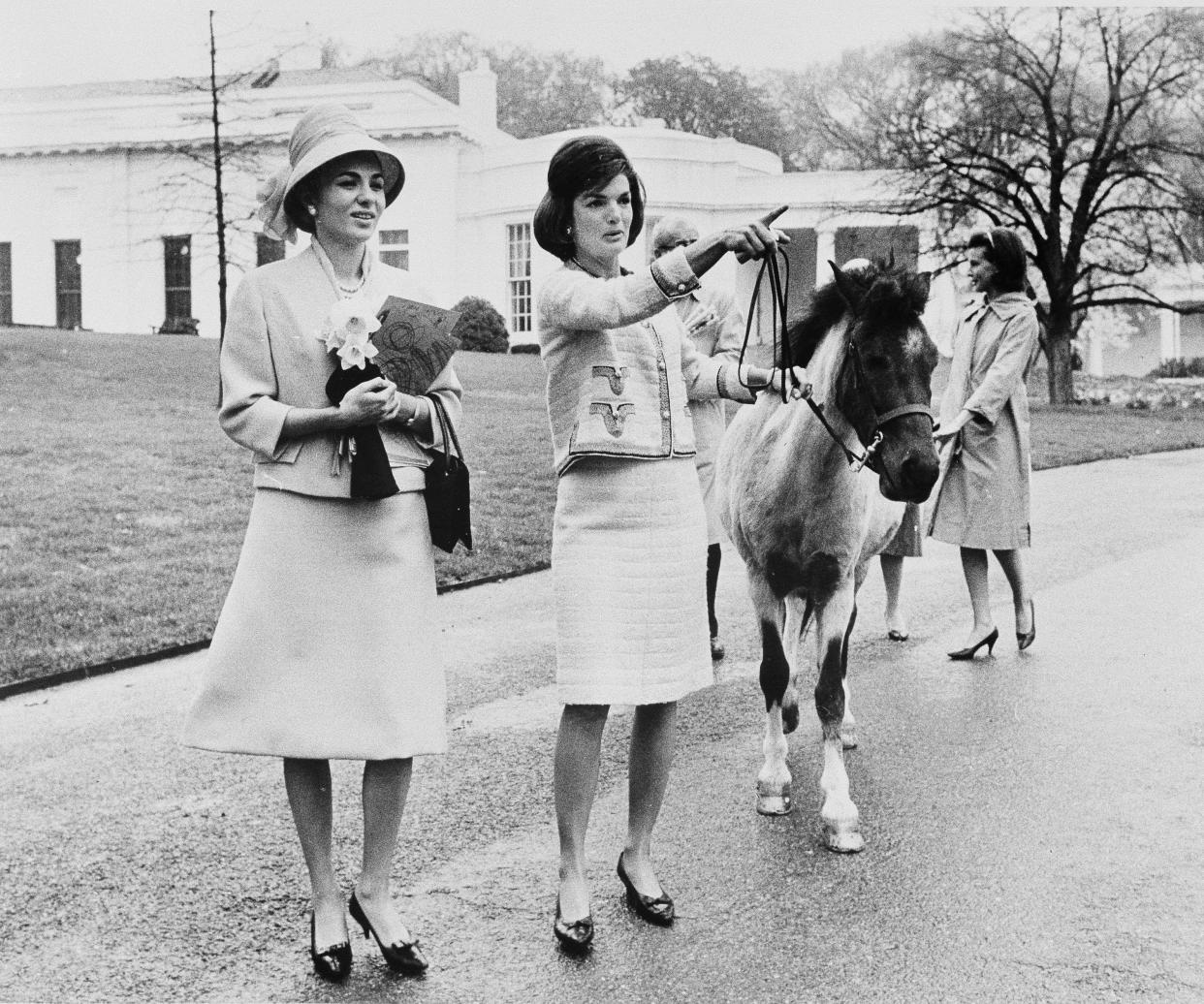 In this April 12, 1962, file photo first lady Jacqueline Kennedy gives a guided tour of the White House grounds to Empress Farah Pahlavi of Iran in Washington. Kennedy leads her daughter Caroline's pony, Macaroni, which had been nuzzling the empress, attracted by the daffodils she was carrying. In the background is the first lady's press secretary, Pamela Turnure. (AP Photo/Pool, File)