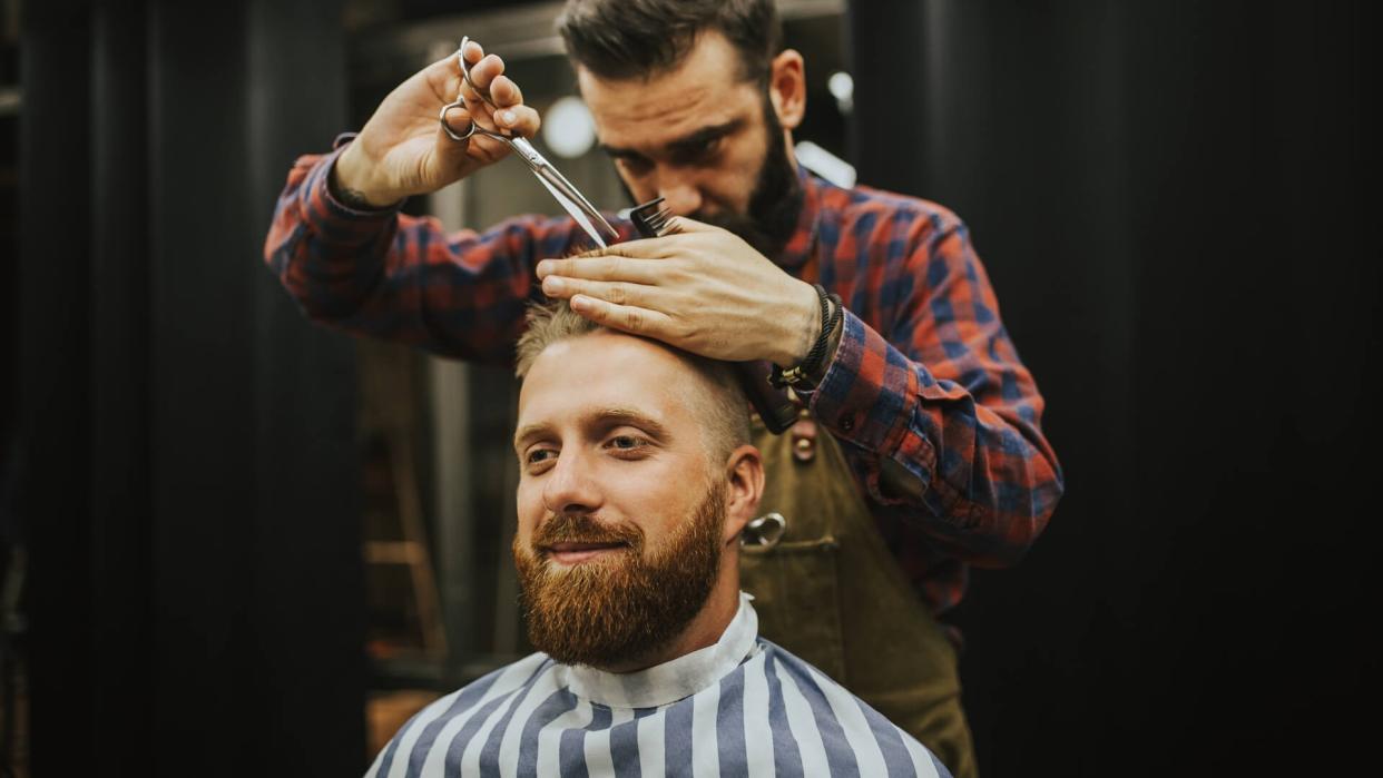 Hipster young good looking man visiting hairstylist in barber shop.