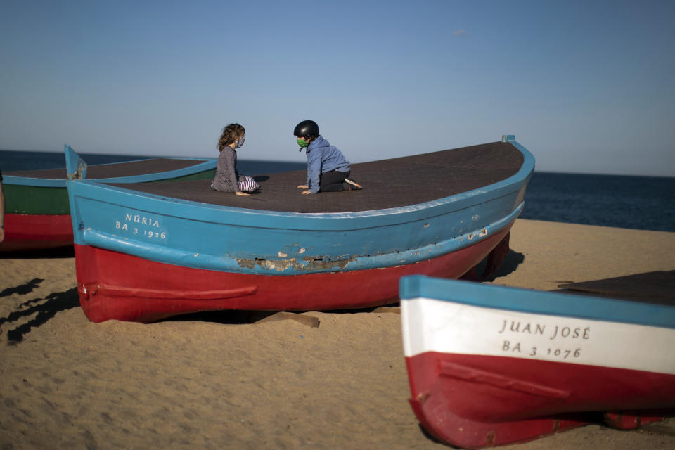 Two children wearing face masks sit on top of a boat in a beach in Badalona, near Barcelona, Spain, Tuesday, April 28, 2020 as the lockdown to combat the spread of coronavirus continues. Health authorities in Spain are urging parents to be responsible and abide by social distancing rules a day after some beach fronts and city promenades filled with families eager to enjoy the first stroll out in six weeks. (AP Photo/Emilio Morenatti)