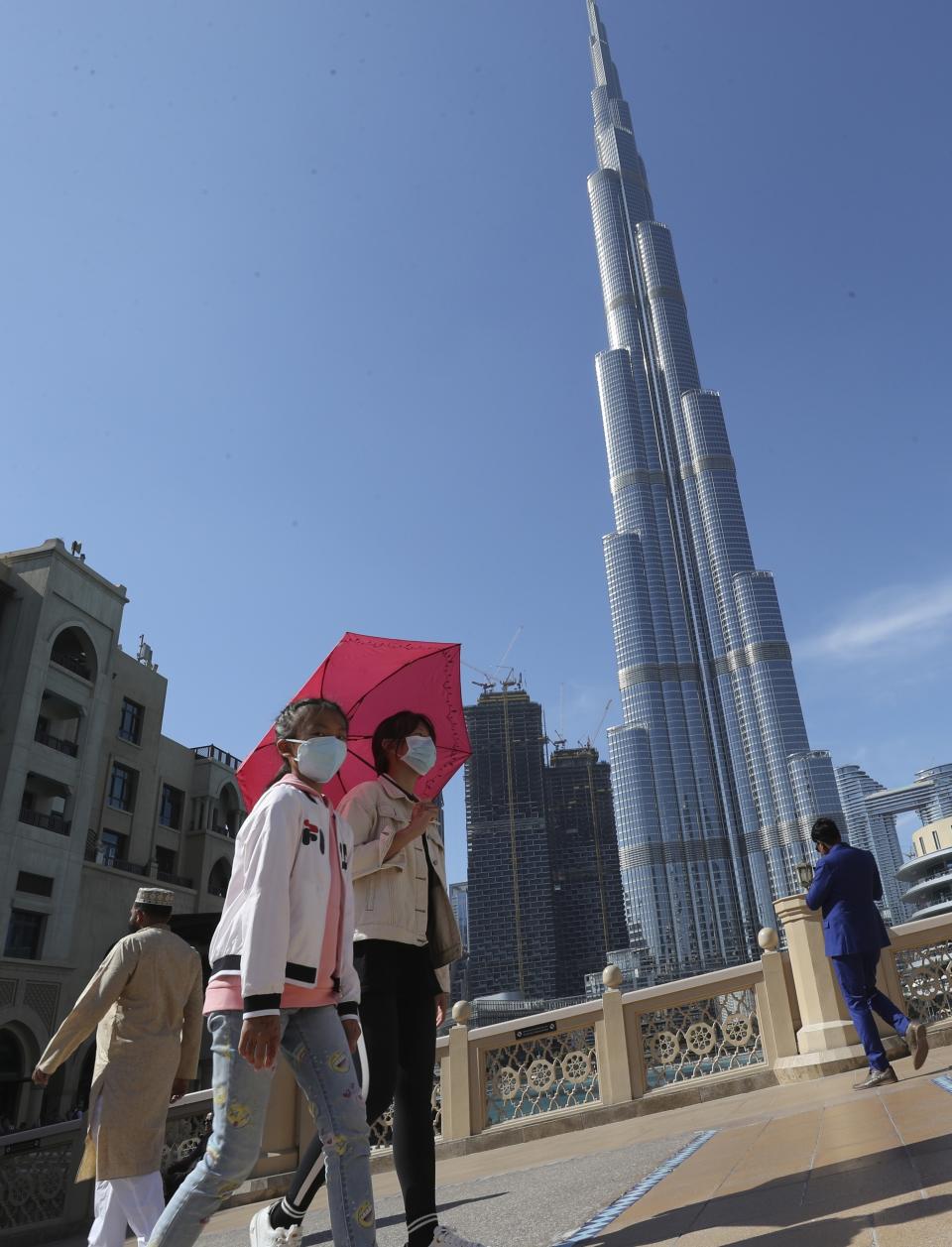In this Thursday, Jan. 30, 2020, photo, Chinese women with face masks walk under the world's tallest tower, Burj Khalifa, in Dubai, United Arab Emirates. The World Health Organization declared the outbreak sparked by a new virus in China that has been exported to more than a dozen countries as a global emergency Thursday after the number of cases spiked tenfold in a week. (AP Photo/Kamran Jebreili)