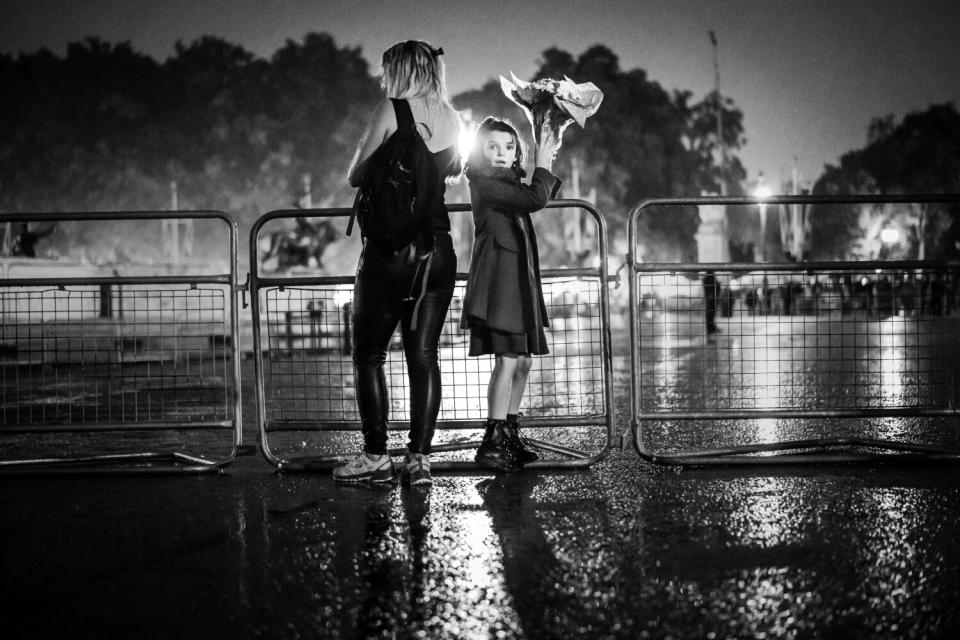 A woman and girl stand on a wet road near a barricade.