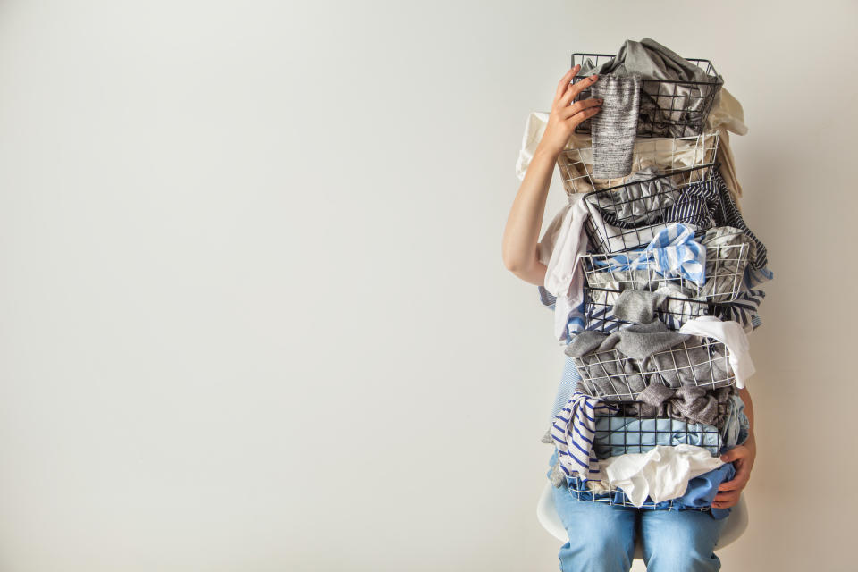 Surprised woman holding metal laundry basket with messy clothes on white background. Laundry. Isolated housewife. Copy space. Textile. Dirty wardrobe. Decluttering concept. Disorganized wife.