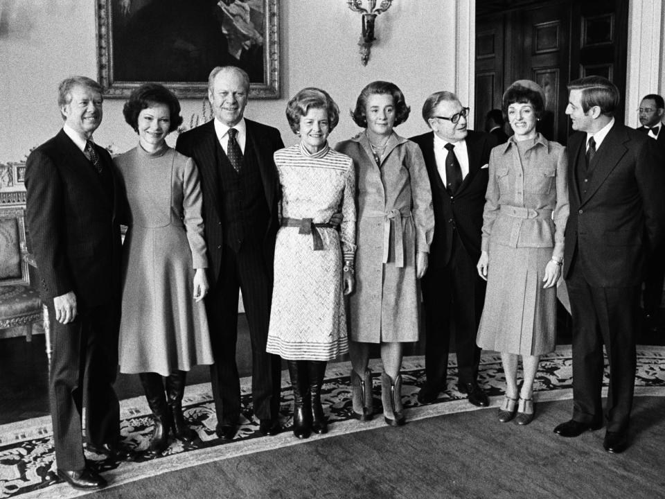 Gerald Ford, Betty Ford in a white striped and belted dress, Jimmy Carter, Rosalynn Carter, Margaretta Rockefeller, Nelson Rockefeller, Joan Mondale and Walter Mondale lined up for a photo.